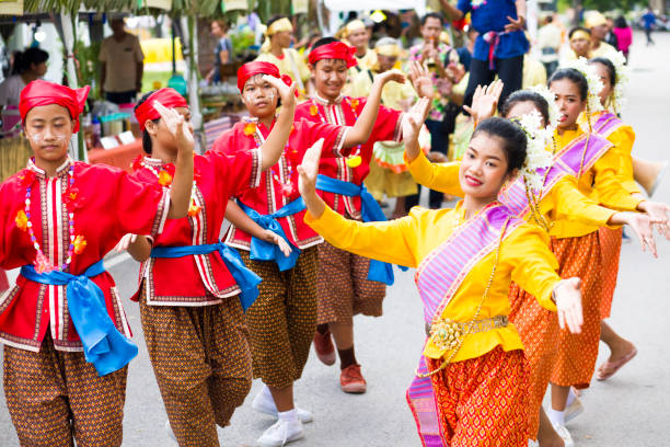 Rows of cheerful Thai Rum thai performing dancing women at Traditional thai festival Rows of cheerful Thai Rum thai performing dancing women at Traditional thai festival in street in Phitsanulok in midnorthern Thailand. Women are dressed in red  and golden traditional clothing and are dancing rum thai while walking along street. There different dressed groups of women. Public local traditional culture event organized by local government. Performance band is dressed traditionally and playing ancient music true thailand classic stock pictures, royalty-free photos & images