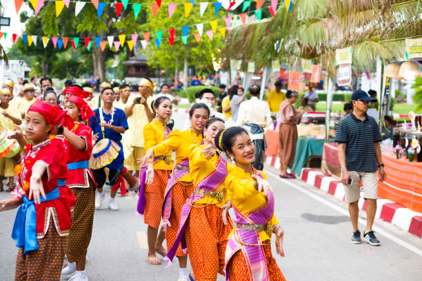 Row of dancing thai women at Traditional thai festival Row of dancing thai women at Traditional thai festival in street in Phitsanulok in midnorthern Thailand. Women are dressed in golden and red traditional clothing and are dancing rum thai while walking along street. There different dressed groups of women. Public local traditional culture event organized by local government. Performance band is dressed traditionally and playing ancient music true thailand classic stock pictures, royalty-free photos & images