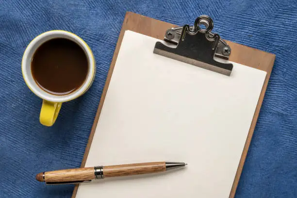 clipboard with a blank paper, desktop flat lay with a cup of coffee and a stylish pen