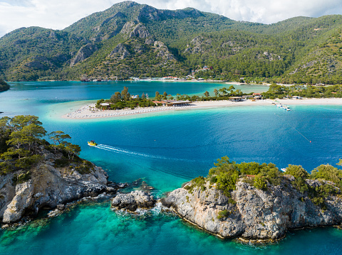 A drone's eye view showcases the breathtaking beauty of Ölüdeniz Beach in Fethiye, Muğla, Turkey. Clear waters, sandy beach, and lush greenery take the spotlight.