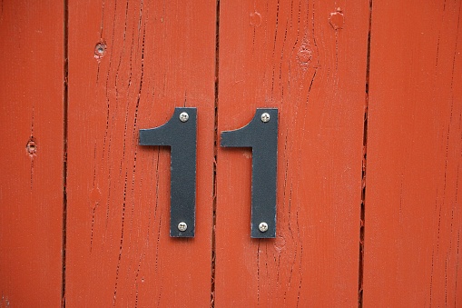 two metal ones are screwed to a red wooden wall and form the house number eleven