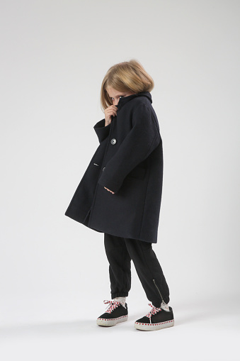 Studio portrait of shyl little girl hiding face behind collar of her coat