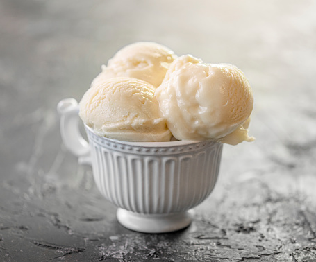 Three balls of creamy ice cream in a white cup on a gray background