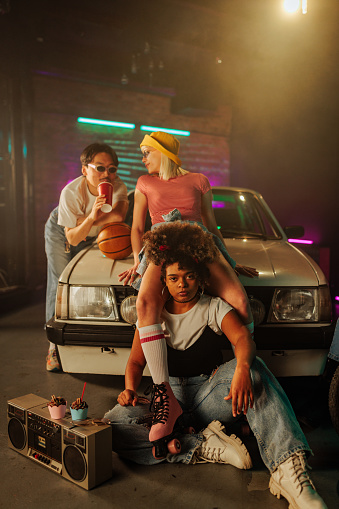 A group of retro stylish friends are socializing outdoors in the evening at the parking lot.