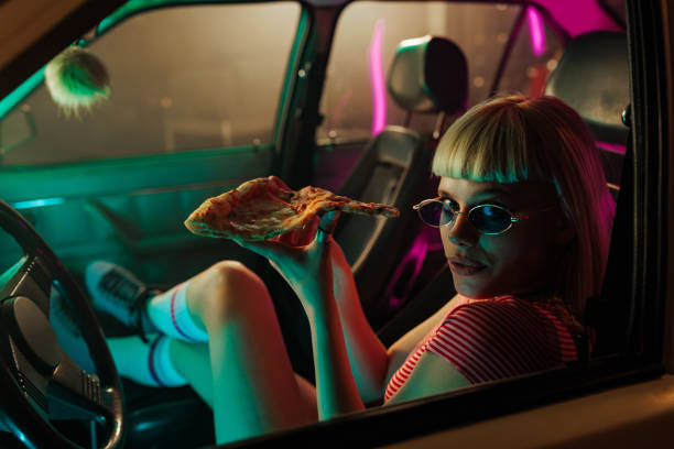 istock Girl eating pizza in car and looking at camera. 1492076643