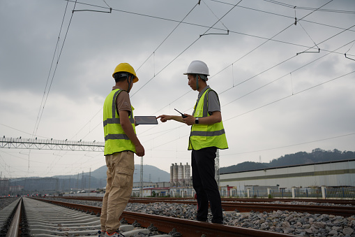 Two railway workers use tablets to check the tracks