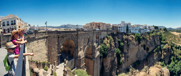 Family sightseeing Ronda, Andalusia, Spain. Mother and little kids are looking at the famous Puente Nuevo bridge in Ronda. \nSunny summer day.\nNikon D810