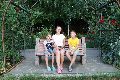 Mother with two her sons sitting on bench in park