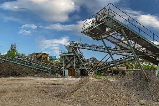 Minning industry gravel quarry conveyor. Crushing machinery, cone type rock crusher, conveying crushed granite gravel stone in a quarry open pit mining.