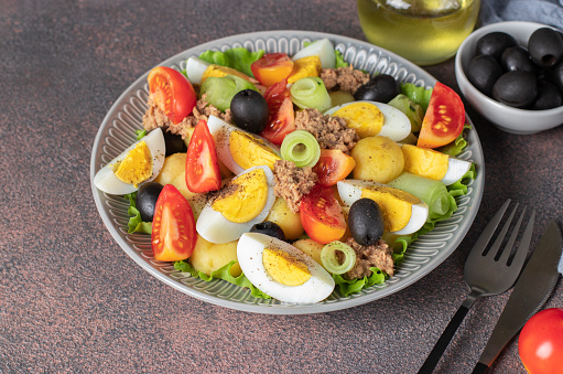 French salad Nicoise with tuna, boiled potatoes, egg, black olives, cucumbers, tomatoes and lettuce on brown background, High angle