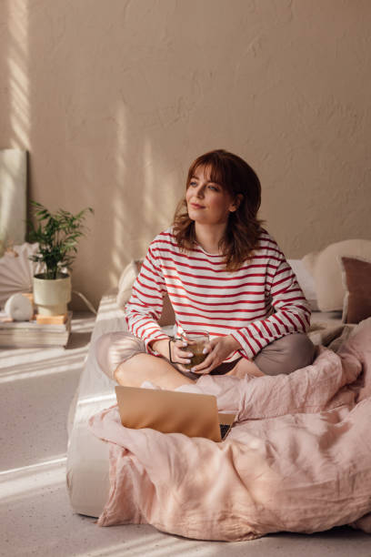 istock Morning Routine: Beautiful Ginger Woman Enjoying a Cup of Coffee in her Bed, while Using her Laptop 1492088147