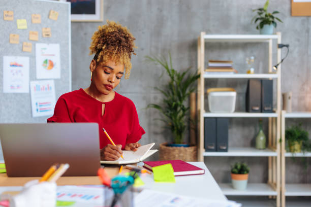 istock African-American business woman looking stressed while writing in notebook in office. 1492089639