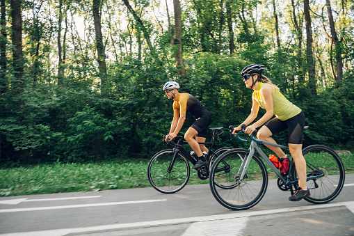 Portrait of a couple wearing sportswear and protective helmet while riding bike outside of the city. Competition and regular training. Riding a race. Copy space.