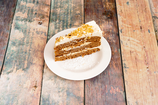 delicious portion of carrot cake with three layers of sponge cake with nuts, two filling and one covering with nuts and icing sugar on a white plate