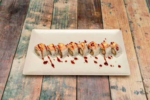 Uramaki dragon roll with flambéed salmon and soy sauce with touches of mayonnaise sauce on white tray