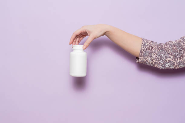 istock White plastic bottle in female hand in lilac background. Packaging for pills, capsules or supplements. 1492103772