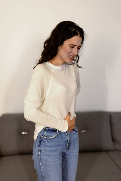 Poor woman with period cramps Poor young Caucasian woman holding her stomach while standing in living room with painful face expression erythema nodosum stock pictures, royalty-free photos & images