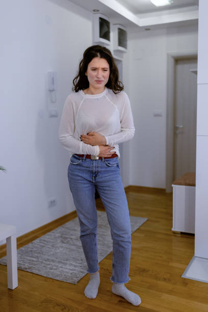 The pain is worsening Sad young Caucasian woman standing and pressing her lower abdomen with painful face expression erythema nodosum stock pictures, royalty-free photos & images