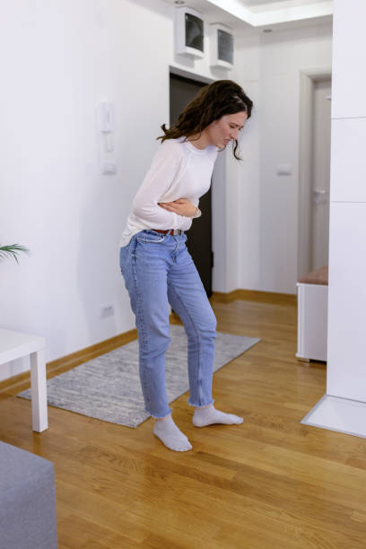 My gut doesn't feel good today Poor young Caucasian woman experiencing stomach pain while standing in a living room at home erythema nodosum stock pictures, royalty-free photos & images