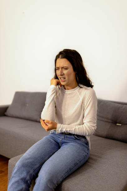 I hit myself so hard Unhappy young Caucasian woman in casual clothing sitting on sofa with painful face expression and touching her elbow erythema nodosum stock pictures, royalty-free photos & images