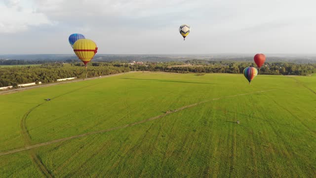 Aerial view of colorful hot air balloons flying over green field