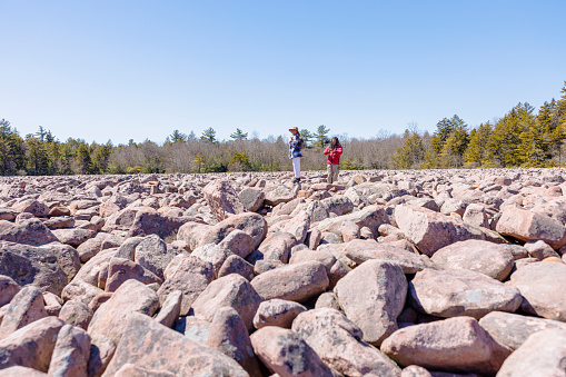 Couple of Latin American man with locks and woman in hat hiking in rock area among sandstones in Hickory Run Boulder Field, Poconos, PA