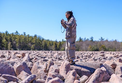 Hispanic tourist exploring Boulder Field - Ice Age geological formation. Man with locks on touristic vacation in mountain area of Hickory Run Boulder Field, Poconos region, Pennsylvania