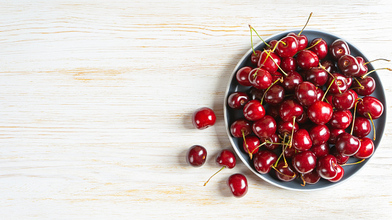 Fresh red ripe sweet cherry on plate on white wooden background. Berry, food background. Top view, banner, header with copy space.