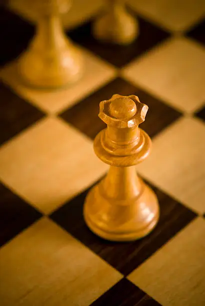 Chess queen with differential focus by firelight on chessboard.