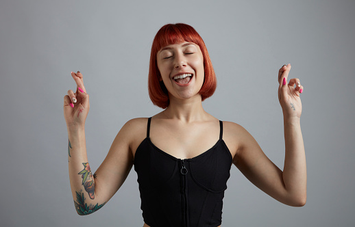 A smiling young woman with short red hair, making a wishing sign with her fingers.