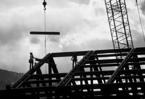 Construction workers guide a beam in position. Backlit B&W