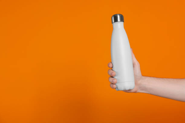 istock Man holding thermo bottle with drink on orange background, closeup. Space for text 1492140095