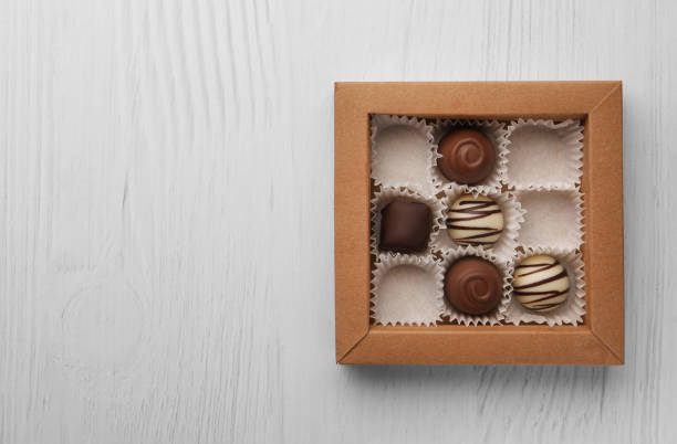 istock Partially empty box of chocolate candies on white wooden table, top view. Space for text 1492141789