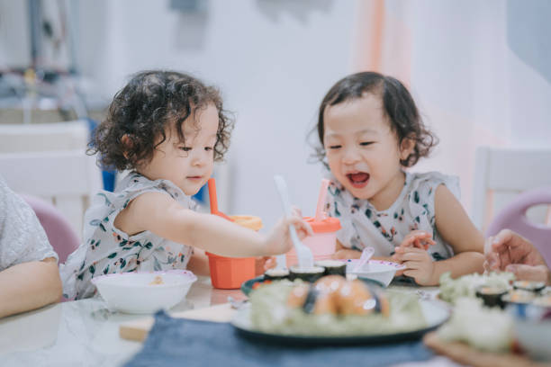 ダイニングルームで食事を楽しむアジア系中国人の一卵性双生児の女の子 - baby child babies only baby girls ストックフォトと画像