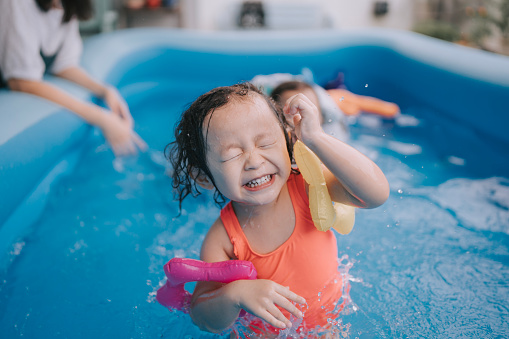 Asian Chinese baby girl enjoying having fun time at backyard in inflatable swimming pool with family during weekend