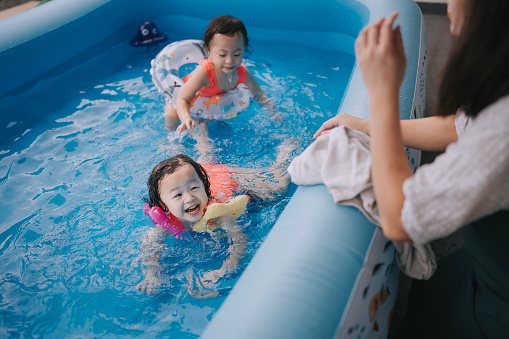 Asian Chinese identical twin baby girls enjoying having fun time at backyard in inflatable swimming pool with family during weekend