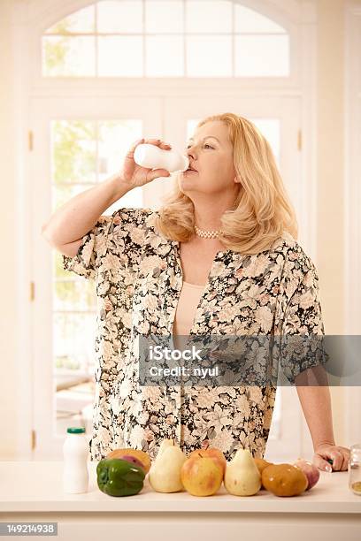 Woman Drinking Yogurt In Kitchen Stock Photo - Download Image Now - 50-59 Years, 55-59 Years, Active Seniors