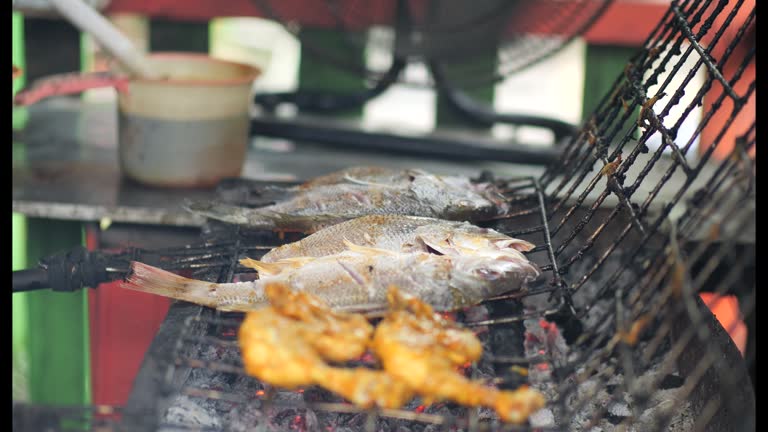 Selective focus of cooking fish. Baking and roasting marinated fish on barbecue grill. Thunnini grilled over charcoal. Summer barbeque hand marinade the fish.