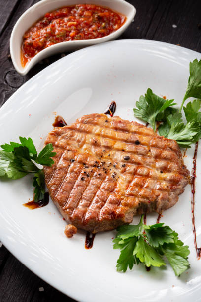 istock Pork meat steak under spicy salsa sauce with greens on a white plate. 1492167800