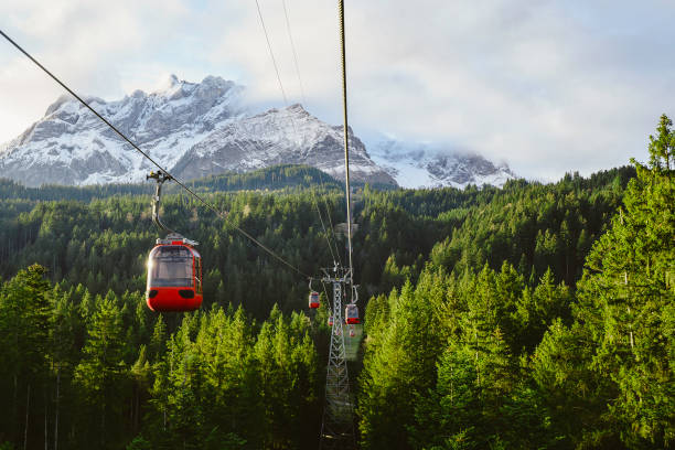 red cable car Surrounded by lush green pines, thick clouds, behind snow-capped mountains, Kriens, Switzerland.
