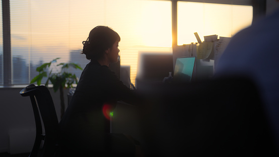 A businesswoman is working in the office during sunset.