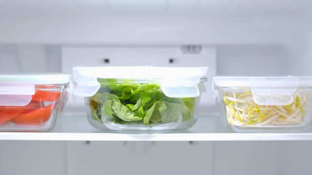 Greens and vegetables in glass containers in the refrigerator, food storage concept.