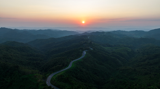 aerial view drone shot ROAD No.1081 or shape number three of winding mountain road between Pua District, Nan Province, Thailand is highlight point and landmark that tourist like to take pictures of because of the beauty of the road, and the sunset for background,