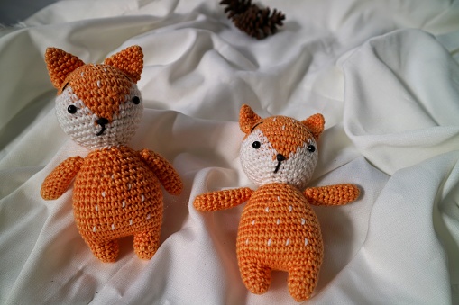 Orange wolf crochet handmade doll made from yarn. Stuffed toy on fluffy background.