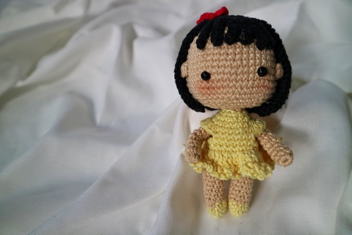 handmade crochet toy, present for baby girl, doll in a yellow dress with red bow on the hair. with short black hair and blush pink on the cheek. Crocheted pretty girl.
