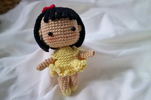 handmade crochet toy, present for baby girl, doll in a yellow dress with red bow on the hair. with short black hair and blush pink on the cheek. Crocheted pretty girl.