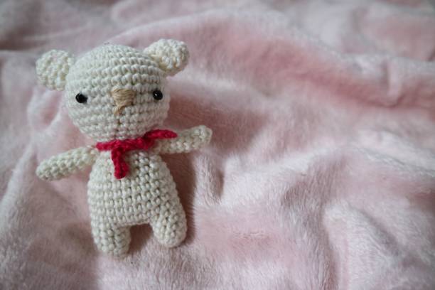 istock Tiny White amigurumi bear on fluffy pink background. Crocheted doll, handmade. Art and craft design. 1492187239