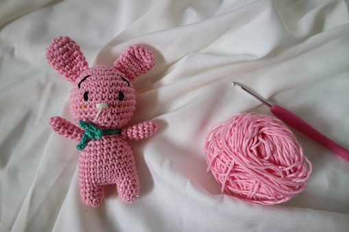 Crocheted rabbit on the white cloth background. Knitted toy, handmade, needlework, bunny amigurumi.