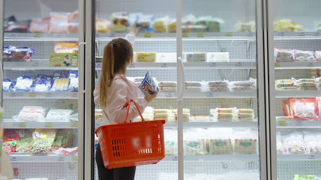 Asian woman picking processed food products from a shelf in a fridge in a department store.