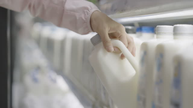 Human hand opening a fridge's door and grabbing a milk gallon.